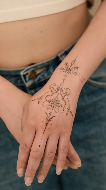 Delicate black-and-grey ornamental floral tattoo across a hand